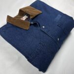 Folded vintage Adolphe Lafont blue denim work jacket showing the brown corduroy collar, metal snaps and chest pockets.